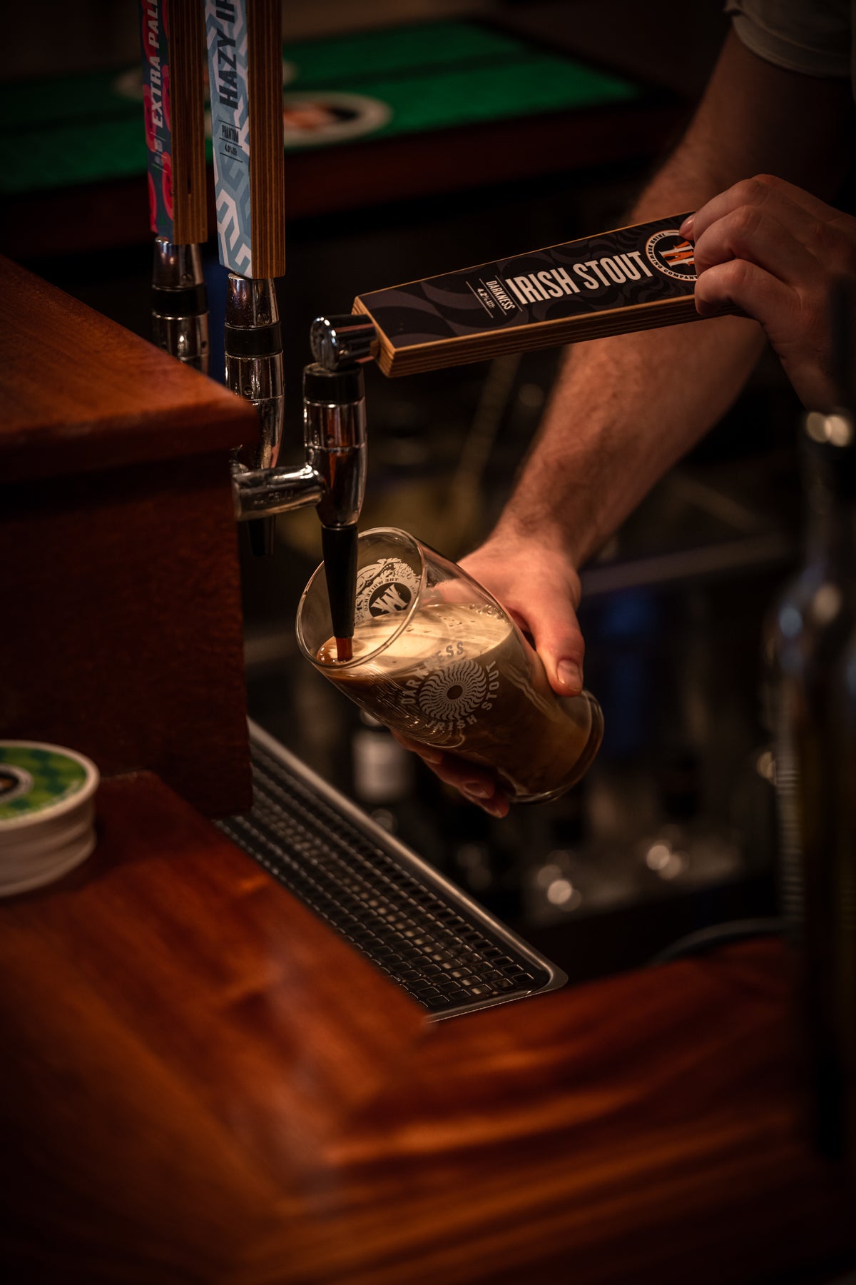 Person pouring a glass of beer from an 'Irish Stout' tap at a bar. Darkness Beer from The Whitee Hag